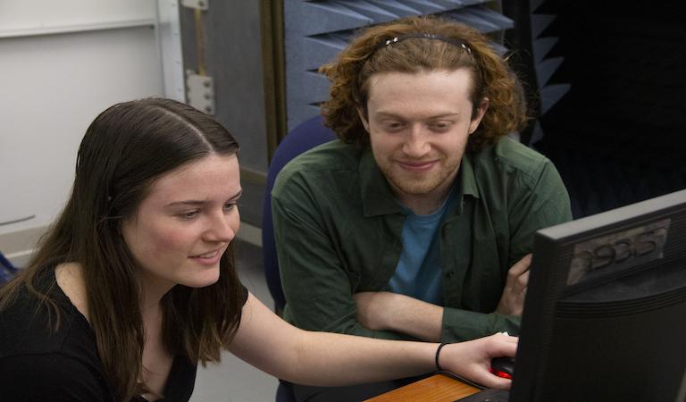 Students sit side by side smiling and looking at a computer screen.